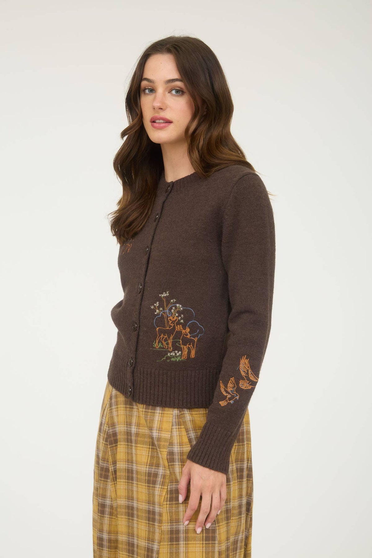Woman wearing a brown embroidered cardigan and plaid skirt on a white background