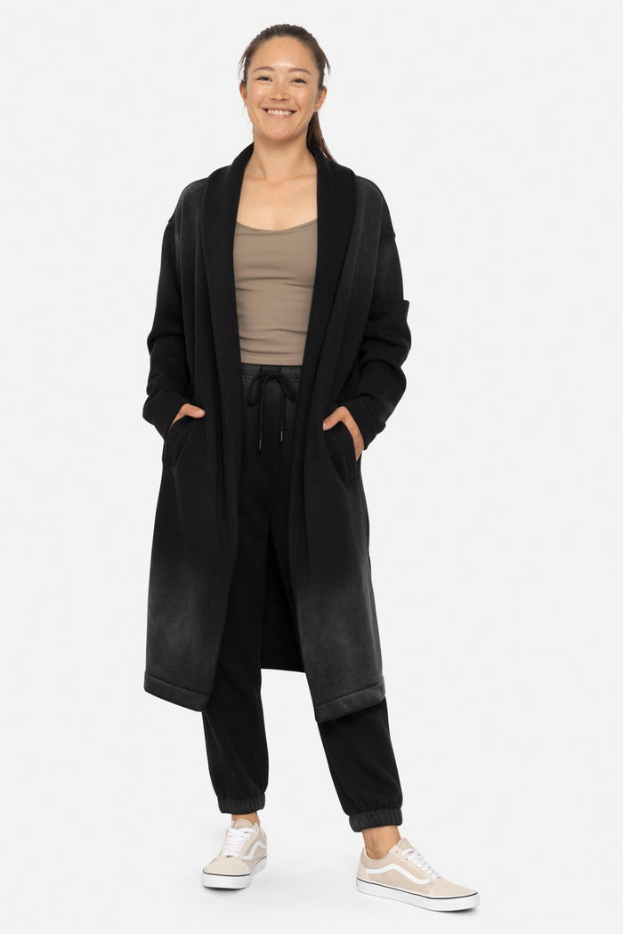 Woman wearing a black long cardigan over a beige top on a white background