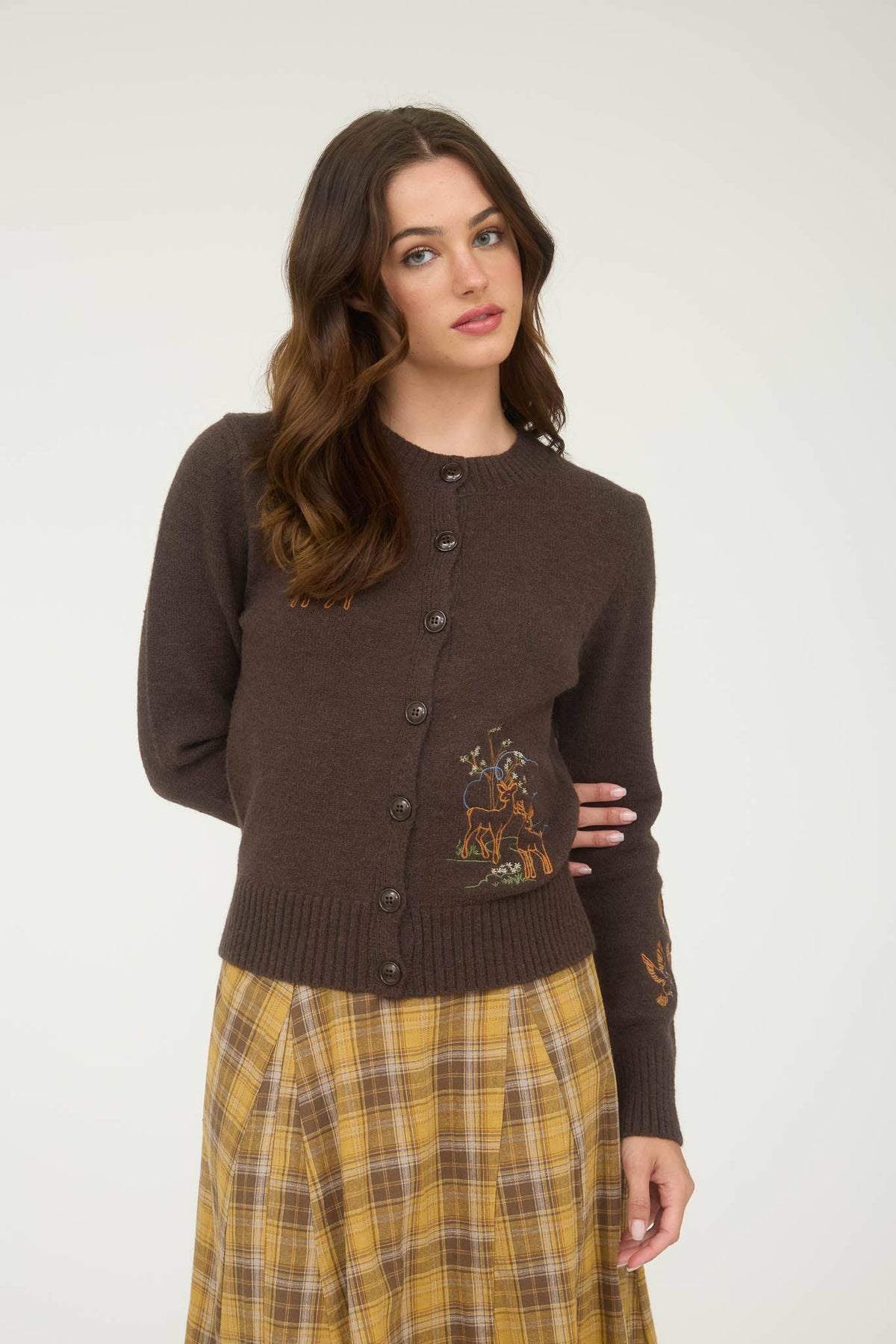 Woman wearing a brown cardigan with embroidery and a plaid skirt on a white background