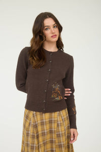 Woman wearing a brown cardigan with embroidery and a plaid skirt on a white background